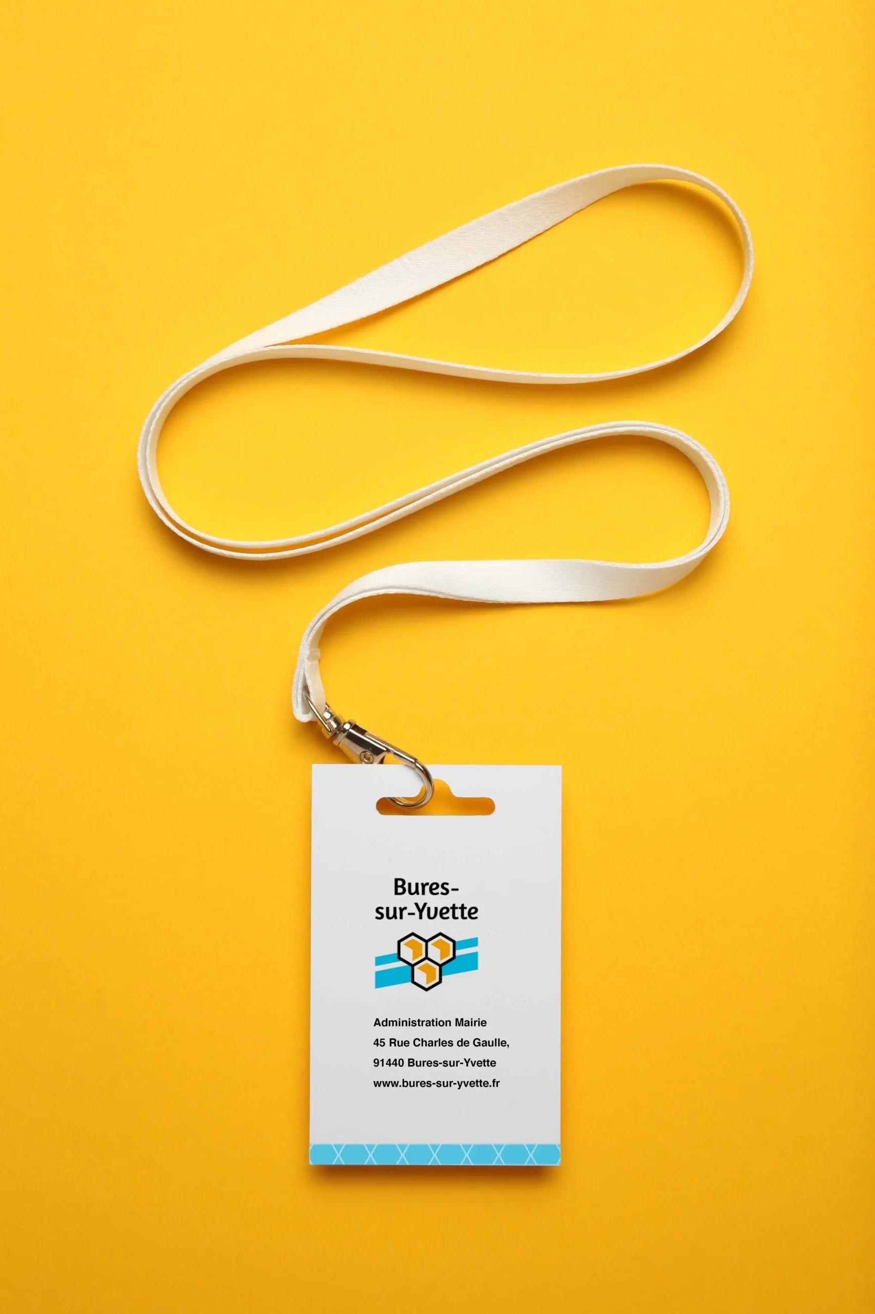 Badge blanc posé sur un fond orange. On y voit le logotype de la ville et la mise en page réalisée (nom, fonction etc.)