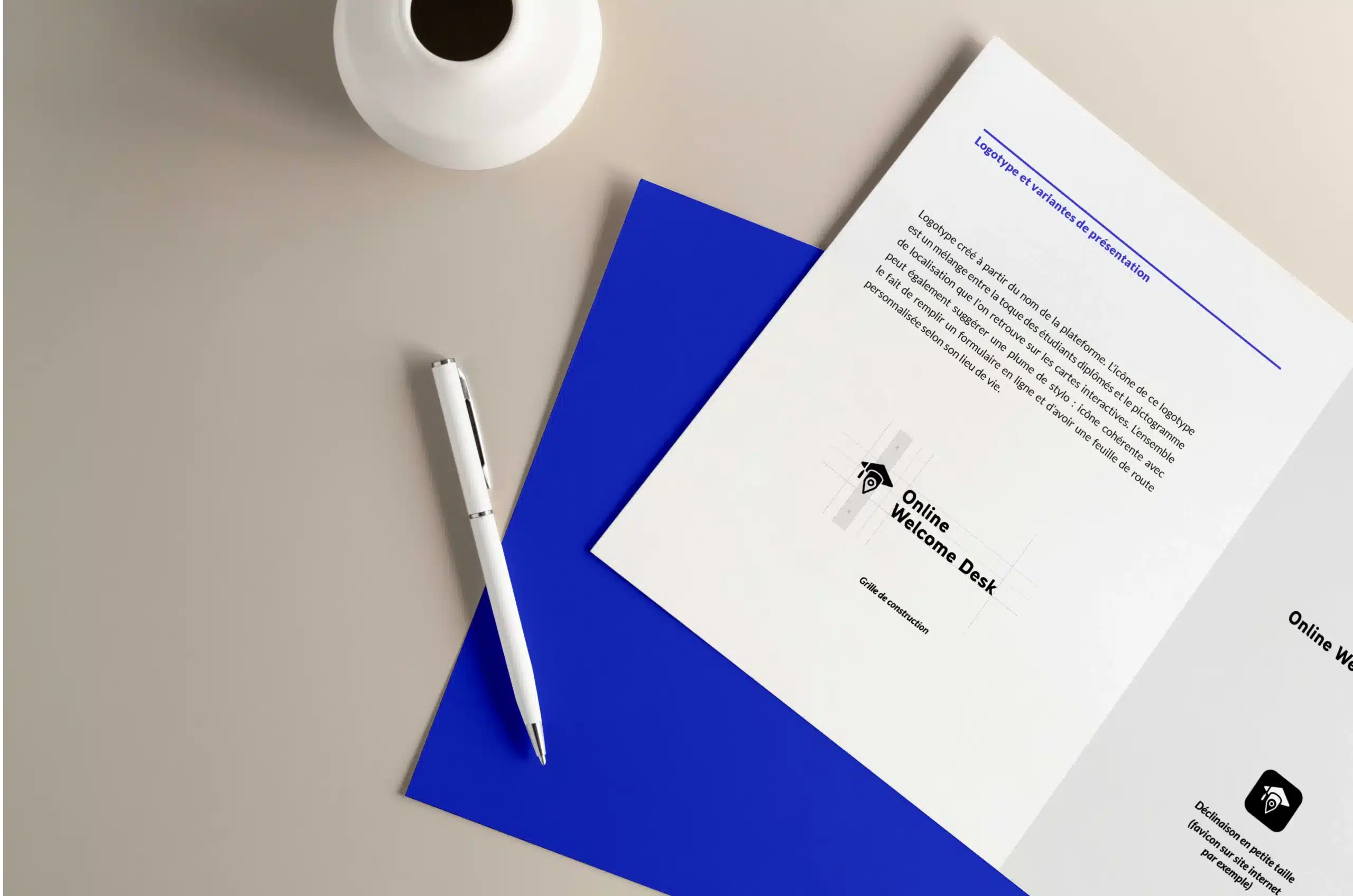 à l'avant de l'image on voit une feuille de papier blanche avec la construction du logotype Online Welcome Desk. À l'arrière on voit une feuille bleu au couleur de la charte graphique