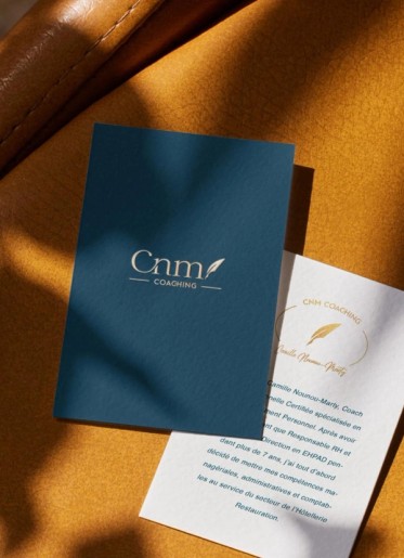 Carte de visite de CNM Coaching avec son logotype en relief, posée sur un fond ocre