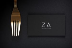 Photo de la carte de visite noir du restaurant Za Paris sur fond noir avec une fourchette posé à côté