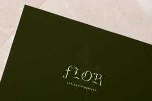 zoom sur une carte de visite du fleuriste Flor. La carte est verte avec le logo en blanc