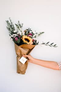 bouquet de fleur tenu par une personne où l'on voi son bras sur la droite. On voit une étiquette avec le logo du fleuriste flor