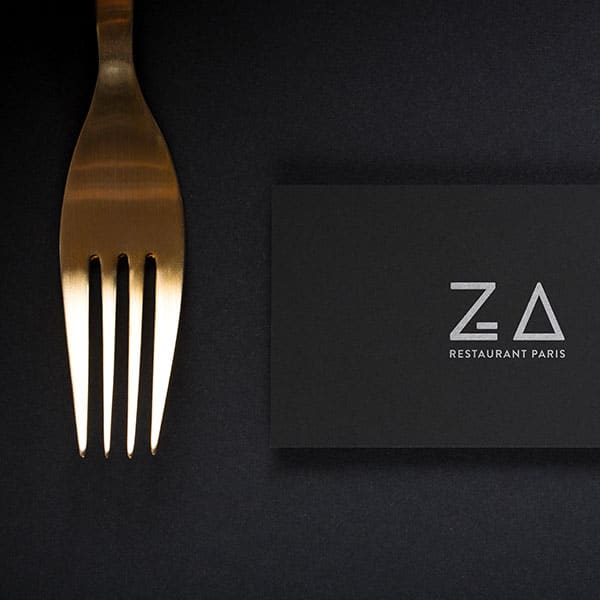 Photo de la carte de visite noir du restaurant Za Paris sur fond noir avec une fourchette posé à côté