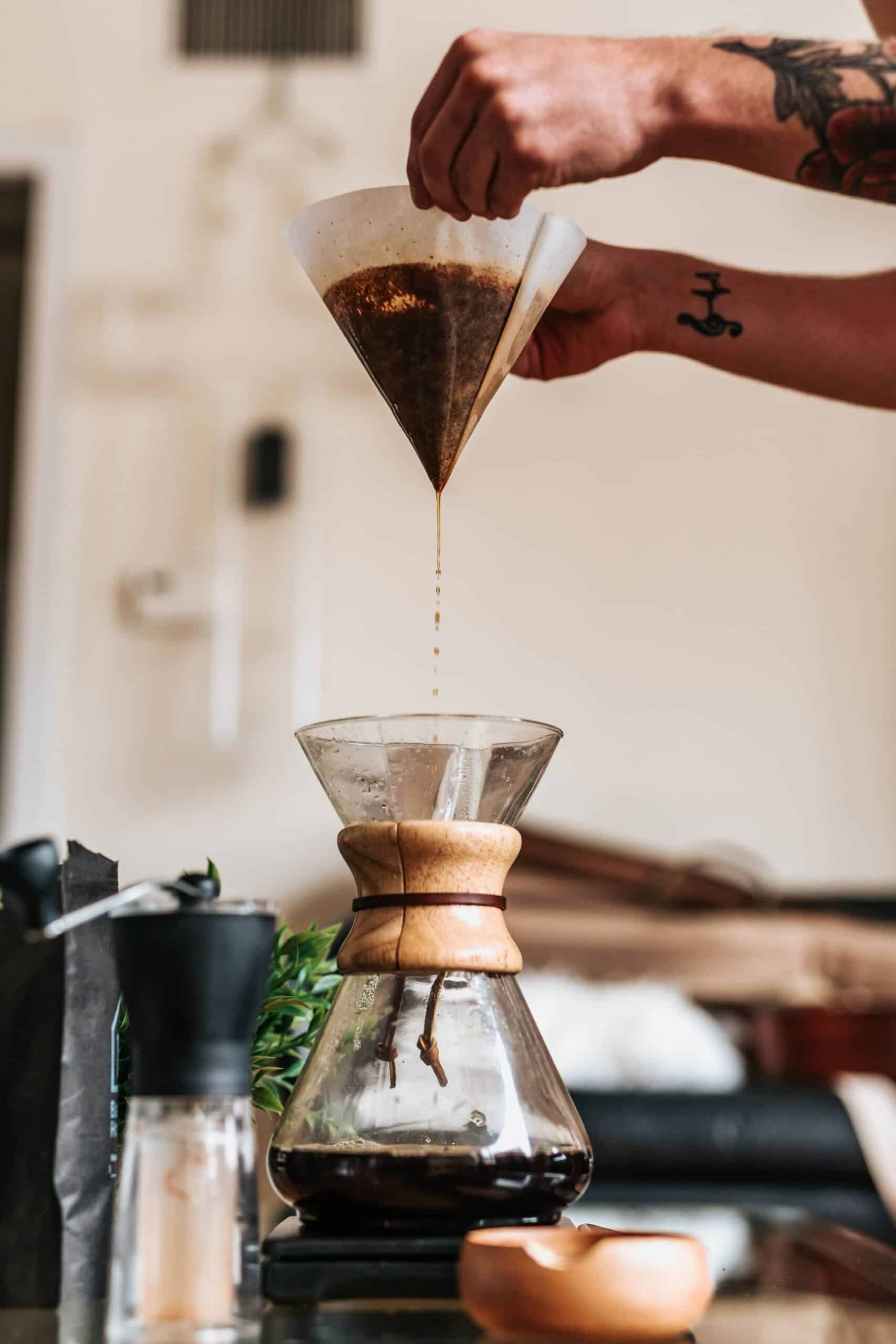 Deux mains qui tiennent un filtre avec du café qui coule dans un pichet