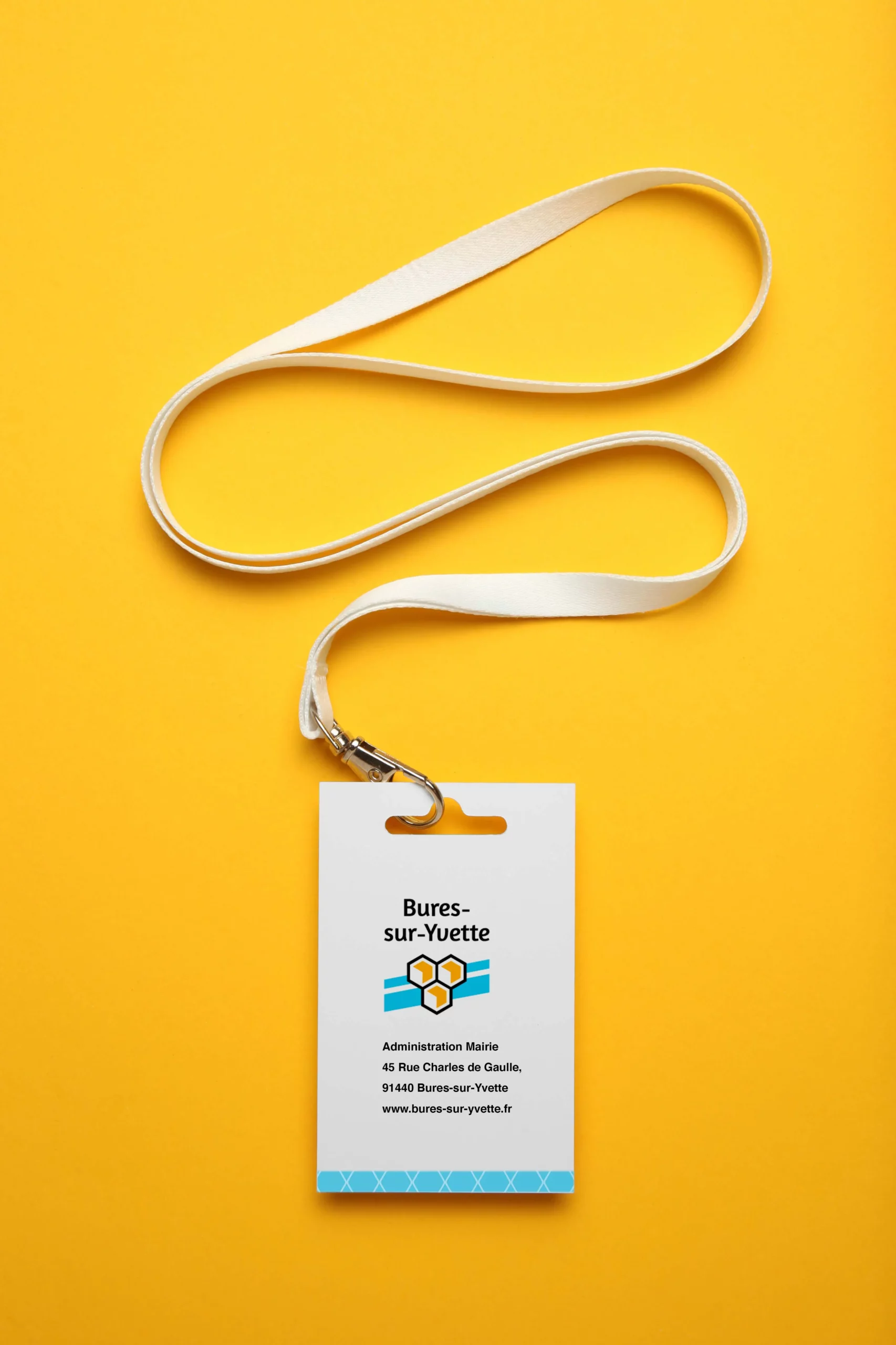 Badge blanc posé sur un fond orange. On y voit le logotype de la ville et la mise en page réalisée (nom, fonction etc.)